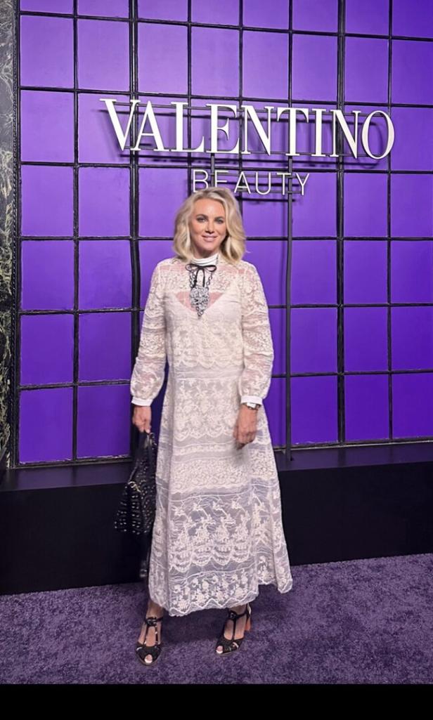 Eine Frau in einem Spitzenkleid posiert vor einem Valentino Beauty Hintergrund.