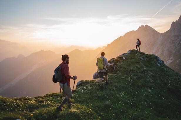Drei Personen erklimmen einen Berg beim Sonnenuntergang.