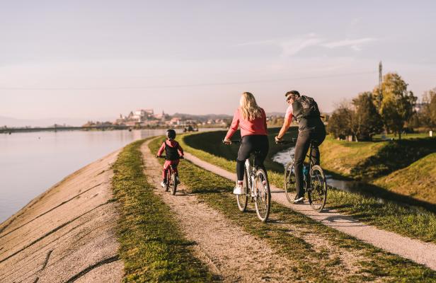 Eine Familie fährt mit Fahrrädern auf einem Weg entlang des Wassers.