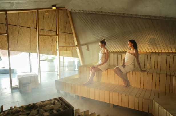 Zwei Frauen sitzen entspannt auf einer Bank in einer Sauna.