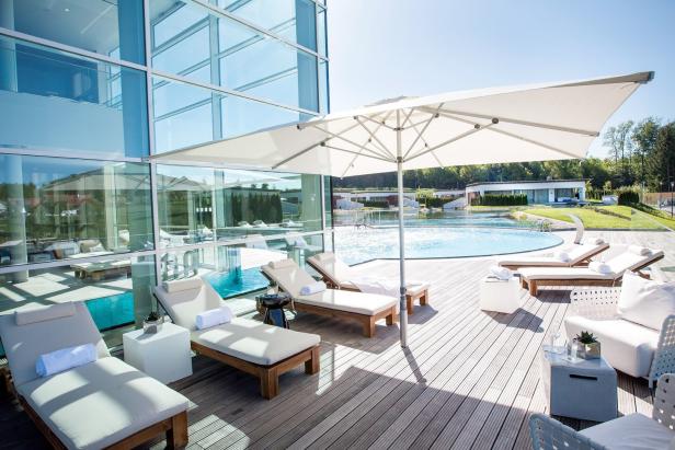 46-Eine Glashalle mit Indoorpool und Auenbecken, davor Liegestühle. Im Hintergrund: die Gästehäuser.