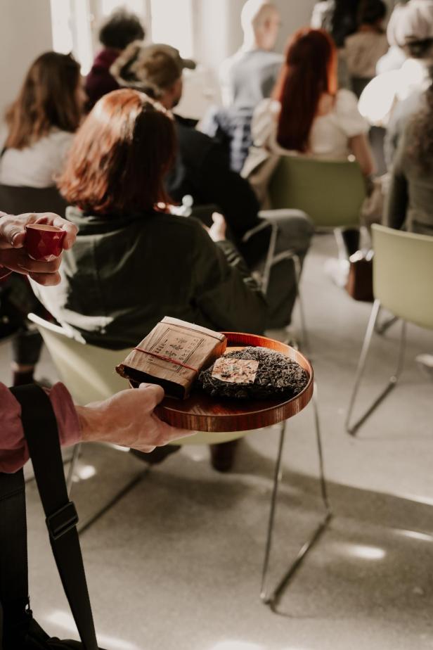 Eine Person präsentiert bei einer Teeverkostung auf dem Vienna Tea Festival einen Pu-Erh-Teekuchen und eine Teepackung auf einem Tablett.