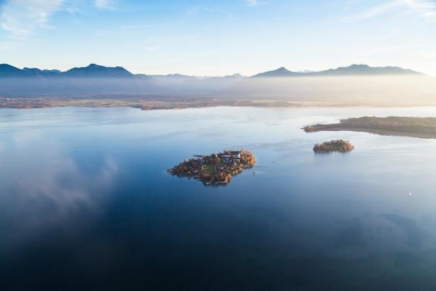 Luftaufnahme eines Sees mit zwei kleinen Inseln und Bergen im Hintergrund unter klarem Himmel.