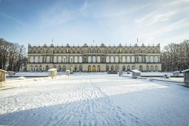 Schloss Herrenchiemsee im Winter mit schneebedecktem Vorplatz und blauem Himmel.