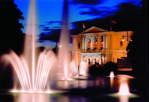 Das Operngebäude von Halle bei Nacht, das von einem Brunnen im Vordergrund umgeben ist