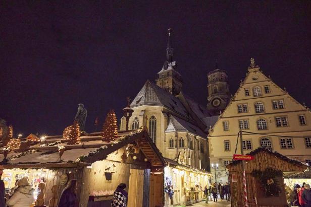 Weihnachtsmarkt mit beleuchteten Holzständen vor historischer Kirche und Fachwerkhaus bei Nacht.