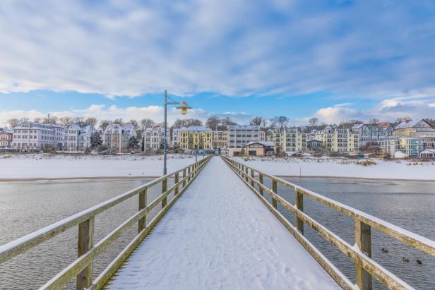Verschneite Seebrücke Bansin mit Blick auf bunte Häuserzeile und winterlichen Himmel.