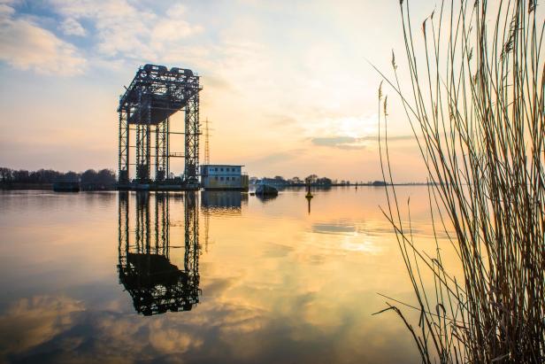 Hubbrücke Karnin über ruhigem Wasser bei Sonnenuntergang, Stahlkonstruktion mit Spiegelung, Schilf am Ufer sichtbar.