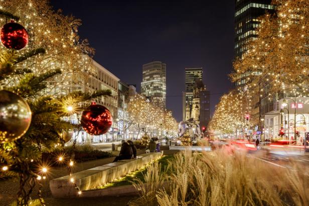 Weihnachtlich geschmückte Straße mit beleuchteten Bäumen, roten und goldenen Kugeln und moderner Architektur im Hintergrund bei Nacht.