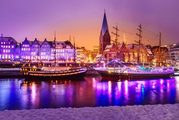 Hafen mit beleuchteten Segelschiffen und historischen Gebäuden vor violettem Abendhimmel in Bremen