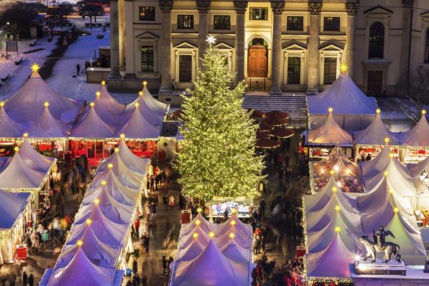 Weihnachtsmarkt mit beleuchtetem Weihnachtsbaum und weißen Zelten vor einem historischen Gebäude bei Nacht in Berlin 