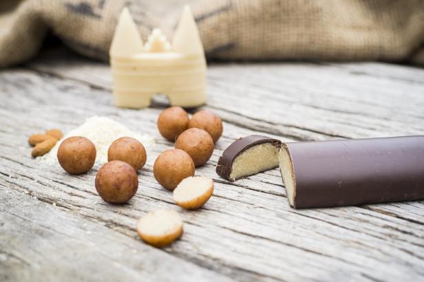 Lübecker Marzipan: Runde, braune Pralinen und eine halbierte Schokoladenpraline mit heller Füllung auf Holzoberfläche, im Hintergrund ein Holzgefäß.