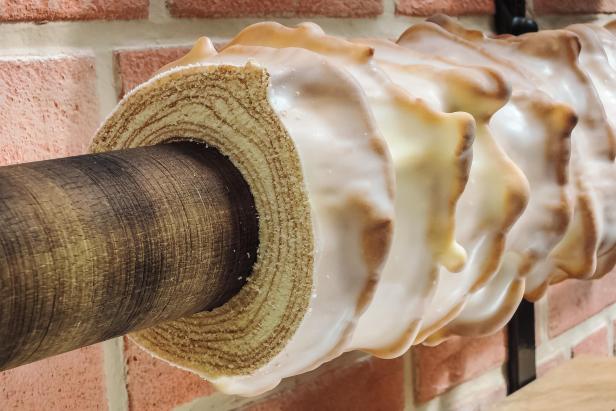 Baumkuchen: Nahaufnahme eines Baumstamms mit Rinde, der in eine runde, schichtweise gebackene Baumkuchenrolle mit Zuckerglasur gesteckt ist.