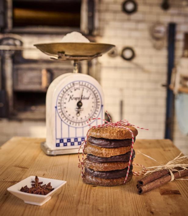 Nürnberger Lebkuchen: Vier mit rotem Band gebundene Lebkuchen vor einer alten Küchenwaage, daneben Zimtstangen und Sternanis auf Holzplatte.