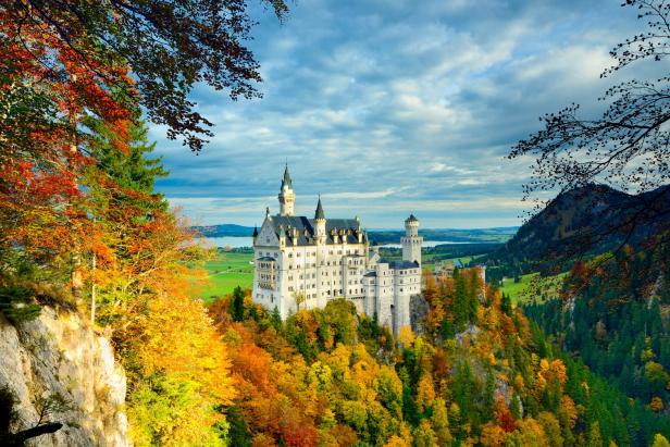 Schloss Neuschwanstein auf bewaldetem Hügel mit buntem Herbstlaub unter bewölktem Himmel