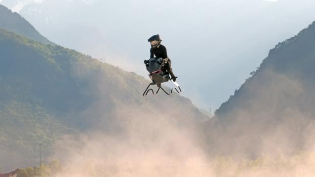 Der Volonaut fliegt durch die Luft, auf ihm sitzt ein Pilot. Das Gerät sieht aus wie eine Mischung aus Motorrad und Motorschlitten.