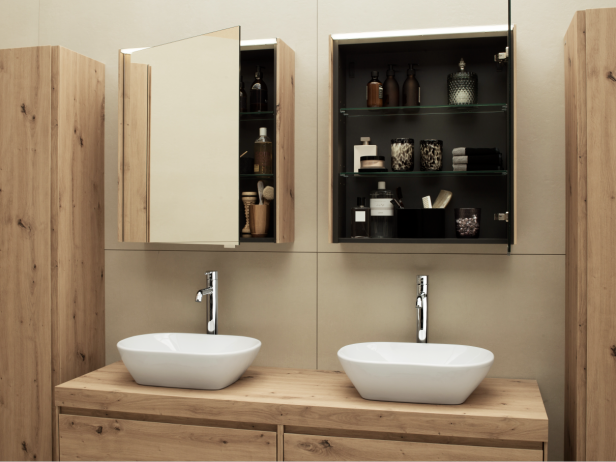 Zwei weiße Waschbecken auf Holzwaschtisch, darüber zwei Spiegelschränke, einer geöffnet mit sichtbaren Pflegeprodukten.