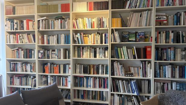 Ein großes Bücherregal, davor ist eine Sitzgelegenheit angeschnitte.