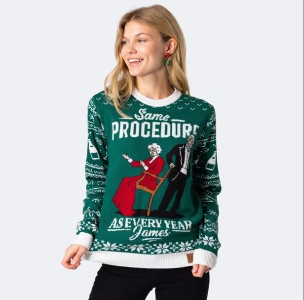 Eine Frau trägt einen grünen Weihnachtspullover mit einem Zitat aus "Dinner for One": "Same procedure as every year, James".
