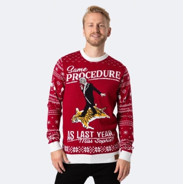 Ein Mann trägt einen roten Weihnachtspullover mit dem Aufdruck aus dem Sketch "Dinner for One": "Same procedure as last year, Miss Sophie?".