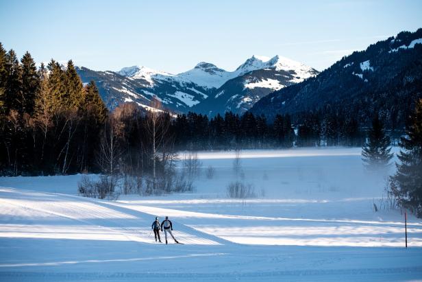 Zwei Langläufer vor dem Schwarzsee in verschneiter Landschaft in Kitzbühel, im Hintergrund erheben sich die Berge.