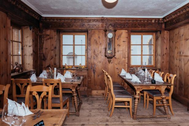 Blick in eine Wirtshausstube: Viele Holzvertäfelungen, eine alte Pendeluhr, alte Stühle und Tische