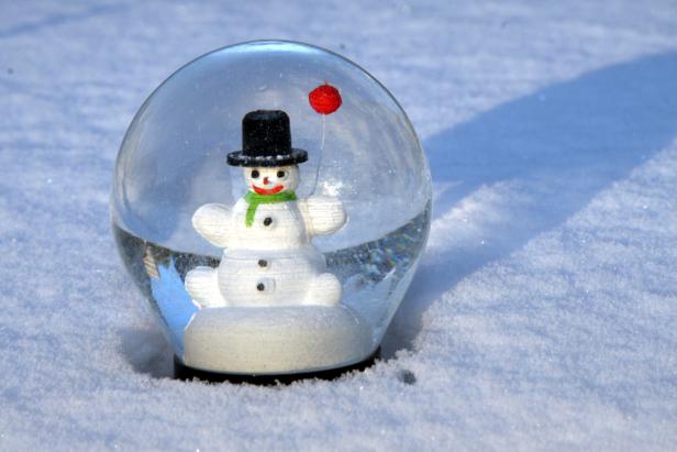 Eine Schneekugel mit einem Schneemann mit Hut und rotem Ballon steht im Schnee.