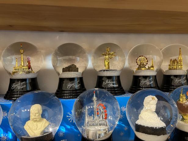 Mehrere Schneekugeln mit Wiener Sehenswürdigkeiten und berühmten Persönlichkeiten stehen nebeneinander auf einem Regal.