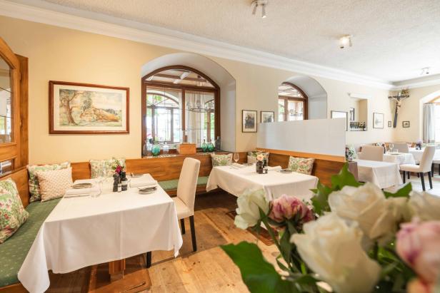 Der einladende Gastraum des Lokals "Das Bräu" mit gedeckten Tischen, Holzbänken und floralen Kissen unter hellen Wänden.