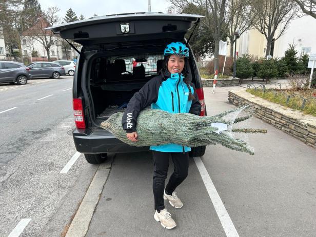 Eine Frau steht vor einem geöffneten Lieferwagen und hält einen Christbaum in der Hand.