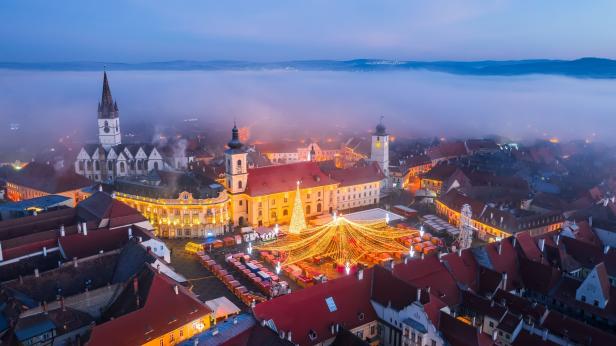 Ein festlicher Weihnachtsmarkt mit Lichterketten auf einem historischen Stadtplatz im Nebel.