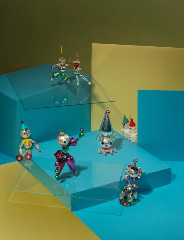 Mehrere bunte Clownfiguren aus Glas und Perlen stehen auf geometrisch angeordneten, farbigen Flächen.