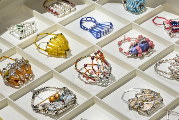 Verschiedene bunte Körbe und Taschen aus Perlen und Draht liegen sortiert in weißen Fächern nebeneinander.