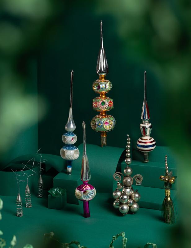 Mehrere bunte und silberne Christbaumspitzen aus Glas und Metall stehen dekorativ auf grünem Untergrund.