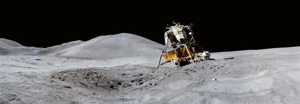 Eine Mondlandefähre steht auf staubiger, grauer Mondoberfläche vor dunklem Himmel und Hügeln.