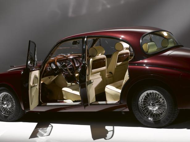 Ein weinrotes Auto mit beigen Ledersitzen und Holzausstattung steht mit geöffneten Türen im Studio.