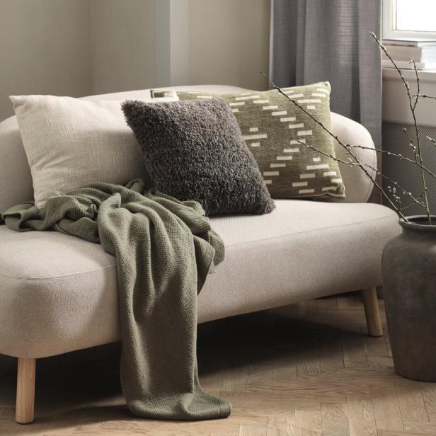 Eine beige Couch mit grünen Kissen und einer grünen Decke drauf.