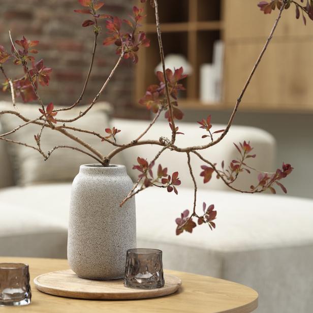 Eine beige Vase mit Zweigen drin. 