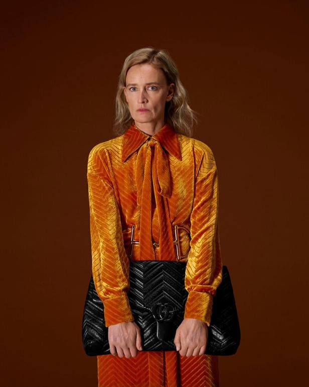 Eine Frau in einer orangen Bluse mit einer schwarzen Tasche in der Hand