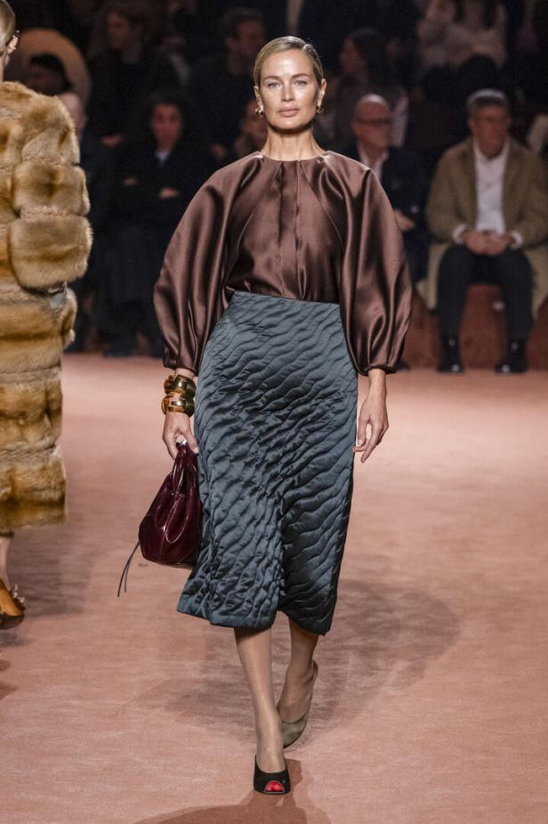 Eine Frau auf dem Laufsteg mit brauner Bluse und grauem Rock. 