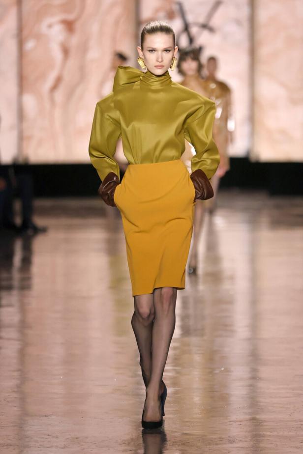 Eine Frau auf dem Laufsteg mit einem gelben Rock und einer grünen Bluse