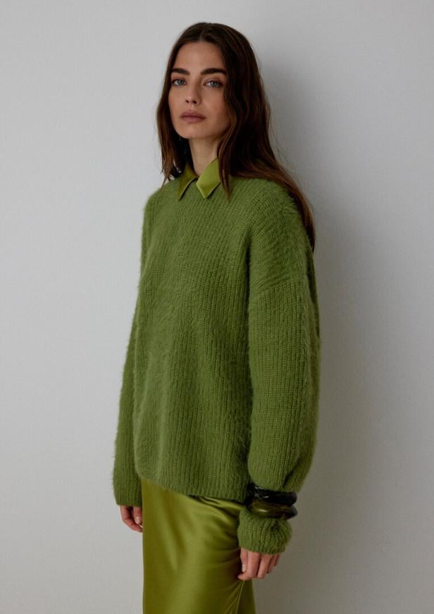 Eine braunhaarige Frau in grünem Pulli und grünem Rock.