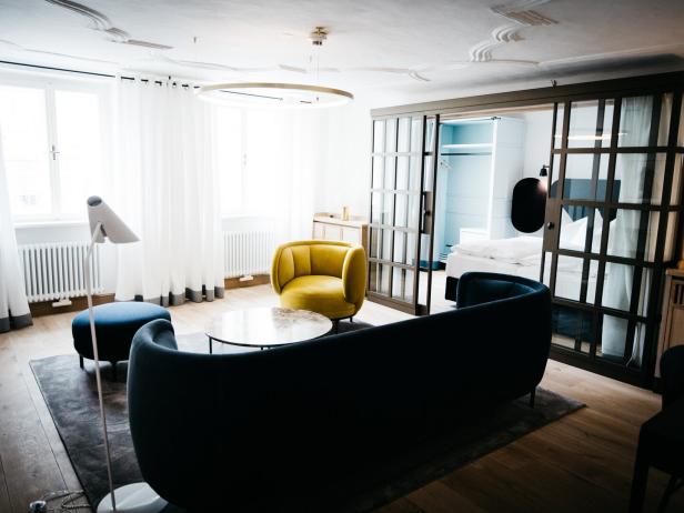 Helles Wohnzimmer mit modernem Sofa, gelbem Sessel, Glastisch und Blick auf ein Schlafzimmer hinter Schiebetüren.