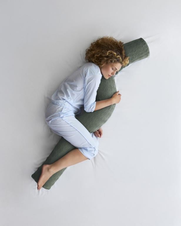 eine Frau im Pyjama, die mit einem grünen Kissen kuschelt