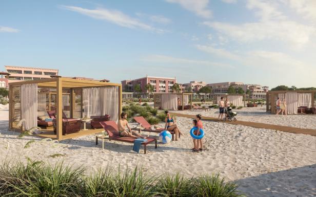 Menschen entspannen auf Liegen und in Pavillons am Sandstrand, Kinder spielen mit einem Ball und Schwimmring, im Hintergrund Gebäude.