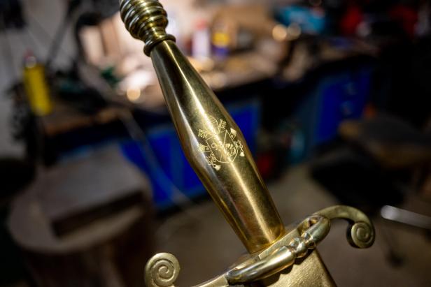 Ein goldener Schwertgriff mit eingraviertem Wappen und detailreichen Verzierungen.