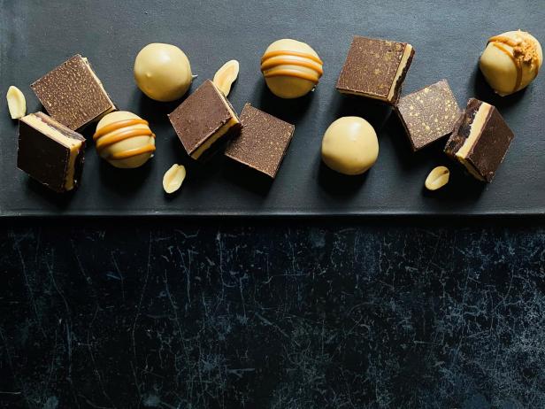 Spekulatius-Pralinen und Erdnuss-Dattel-Konfekt liegen dekorativ mit Erdnüssen auf einer dunklen Platte.