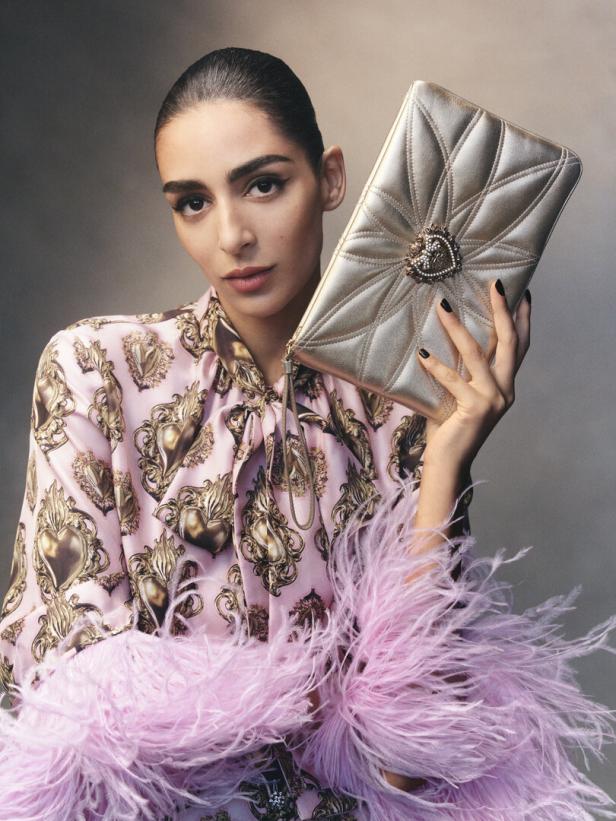 Eine frau in einem lila Kleid mit Federn und einer goldenen Tasche in der Hand 
