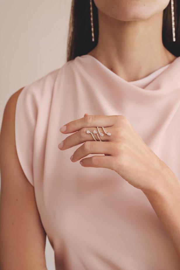 Eine Frau im rosa Kleid mit einem silbernen Ring am Finger, den sie in die Kamera hält