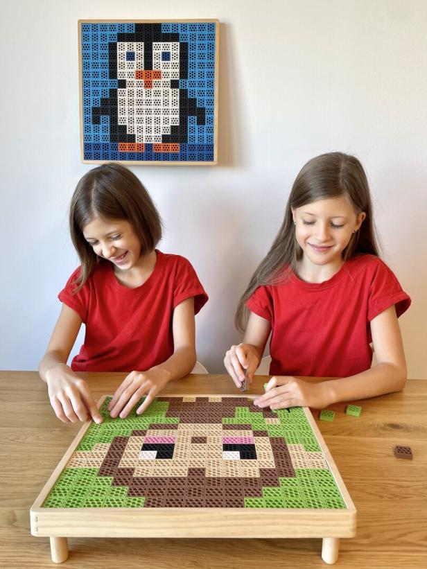 2 Kinder in einem roten Shirt die ein Wandbild basteln 